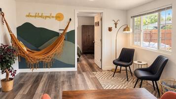 A room with a hammock, a dining table, two chairs, a lamp, and a wall with a deer head decoration.