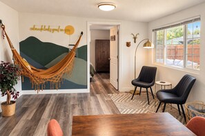 A room with a hammock, a dining table, two chairs, a lamp, and a wall with a deer head decoration. - 5 BR | Hot Tub•Game Room•Fire Pit•Big Backyard (Westminster)