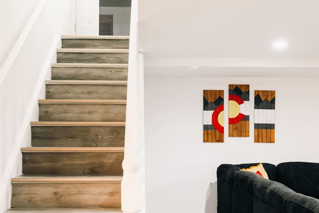 A staircase with wooden steps leading to a landing, a black sofa, and three wall-mounted artworks.
