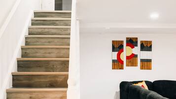 A staircase with wooden steps leading to a landing, a black sofa, and three wall-mounted artworks.