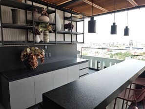Une cuisine moderne avec un plan de travail noir, des armoires blanches et une vue sur la ville depuis un balcon.