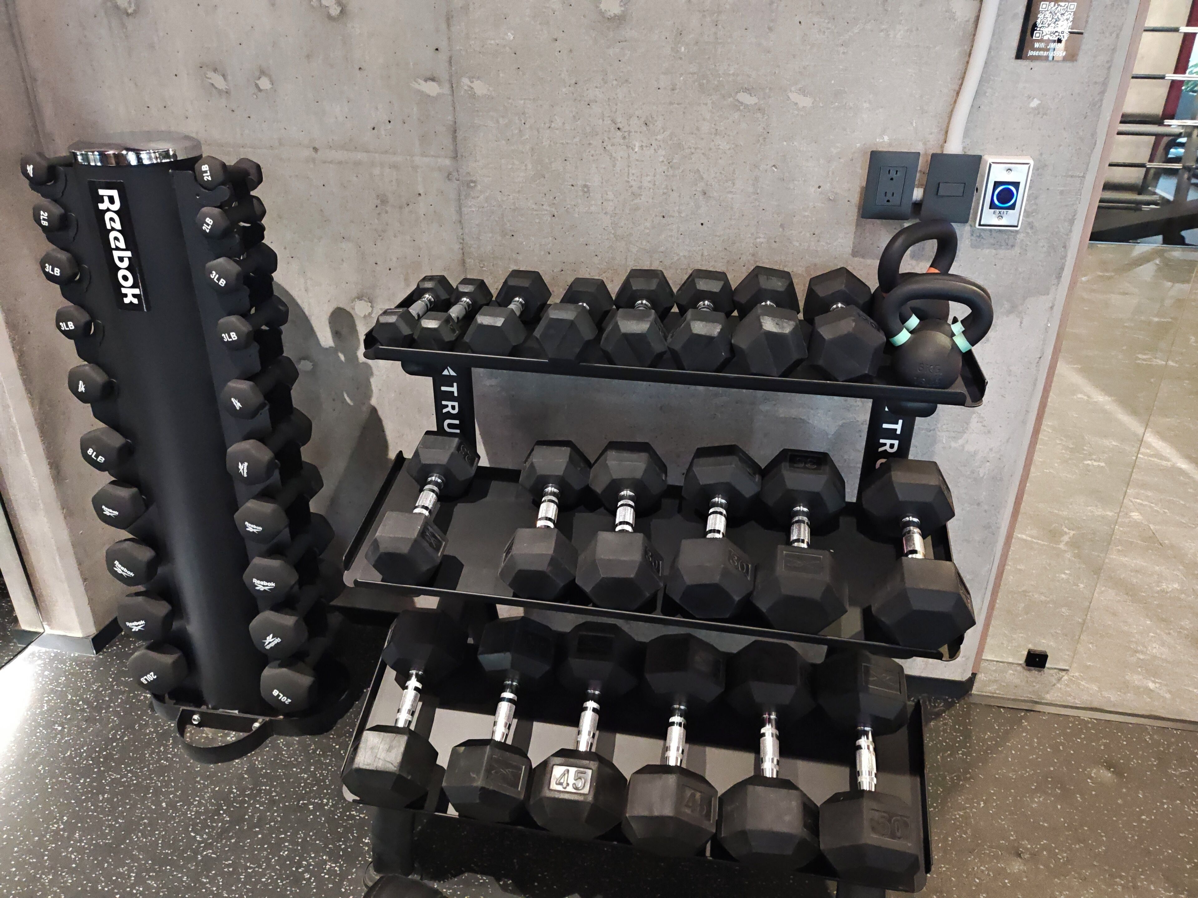 Equipamento de musculação com halteres variados e um banco de supino Reebok.
