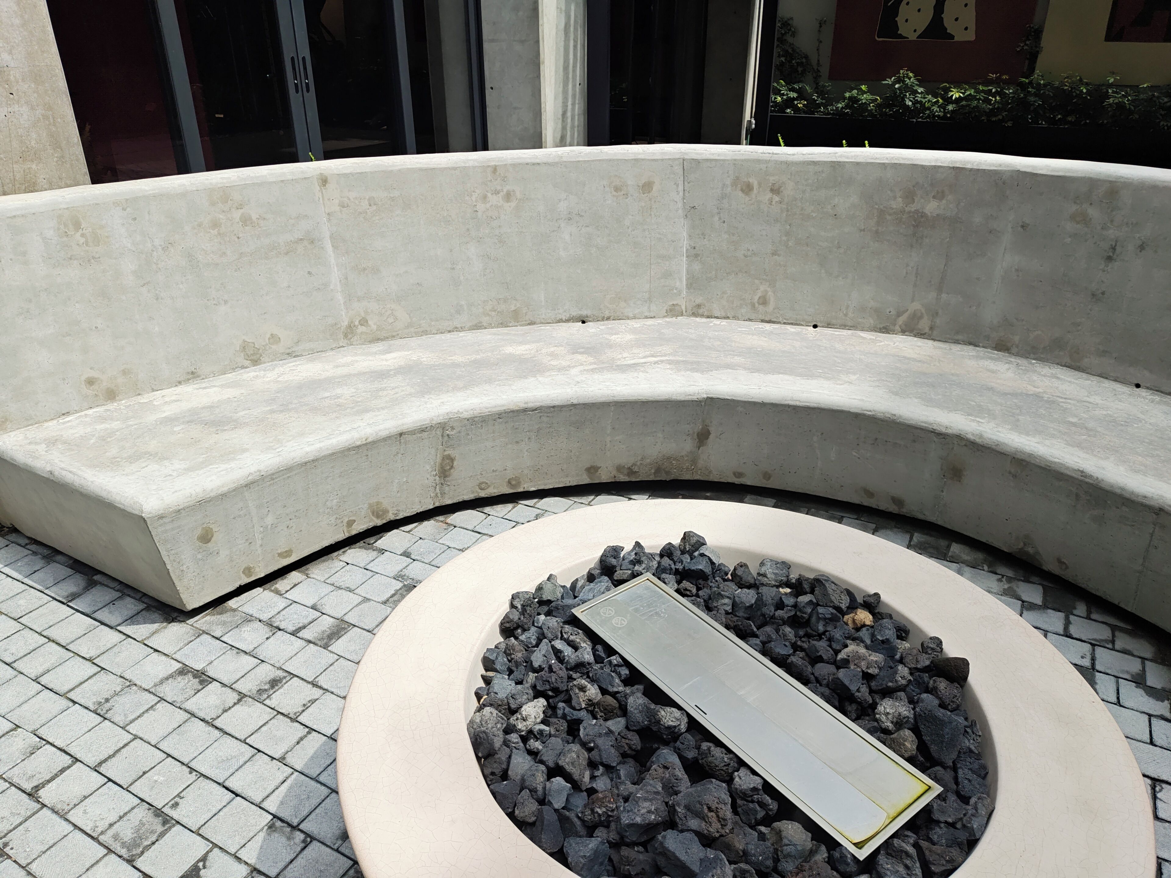 Un banc en béton incurvé, doté d’une assise circulaire agrémentée de rochers et d’une surface réfléchissante.