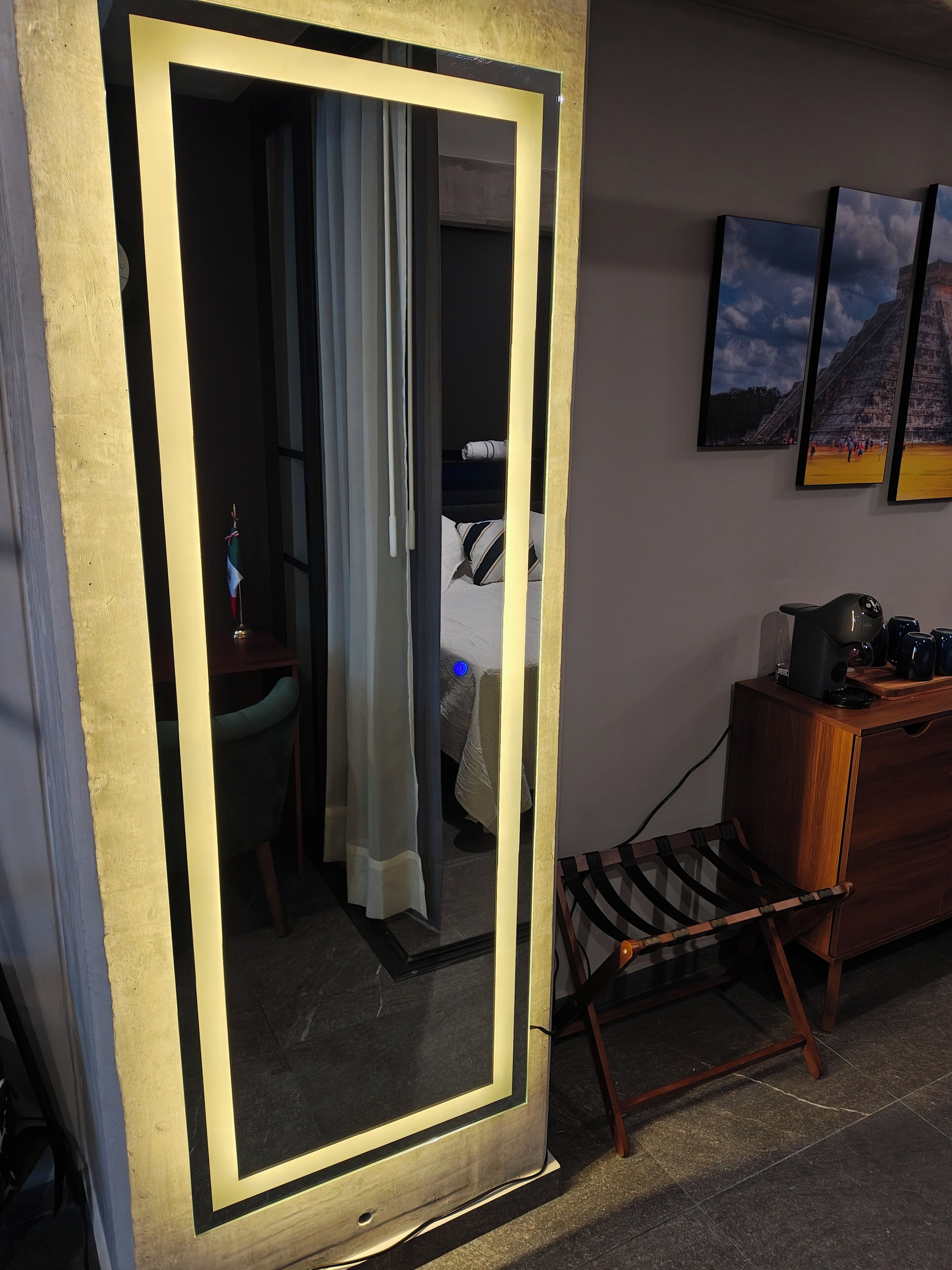 Une chambre d’hôtel avec un grand miroir, un lit doté d’un éclairage bleu, une commode en bois et une chaise.