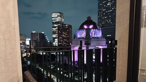 Un balcón con vista a un paisaje urbano nocturno, incluyendo edificios iluminados y una estructura en forma de cúpula.