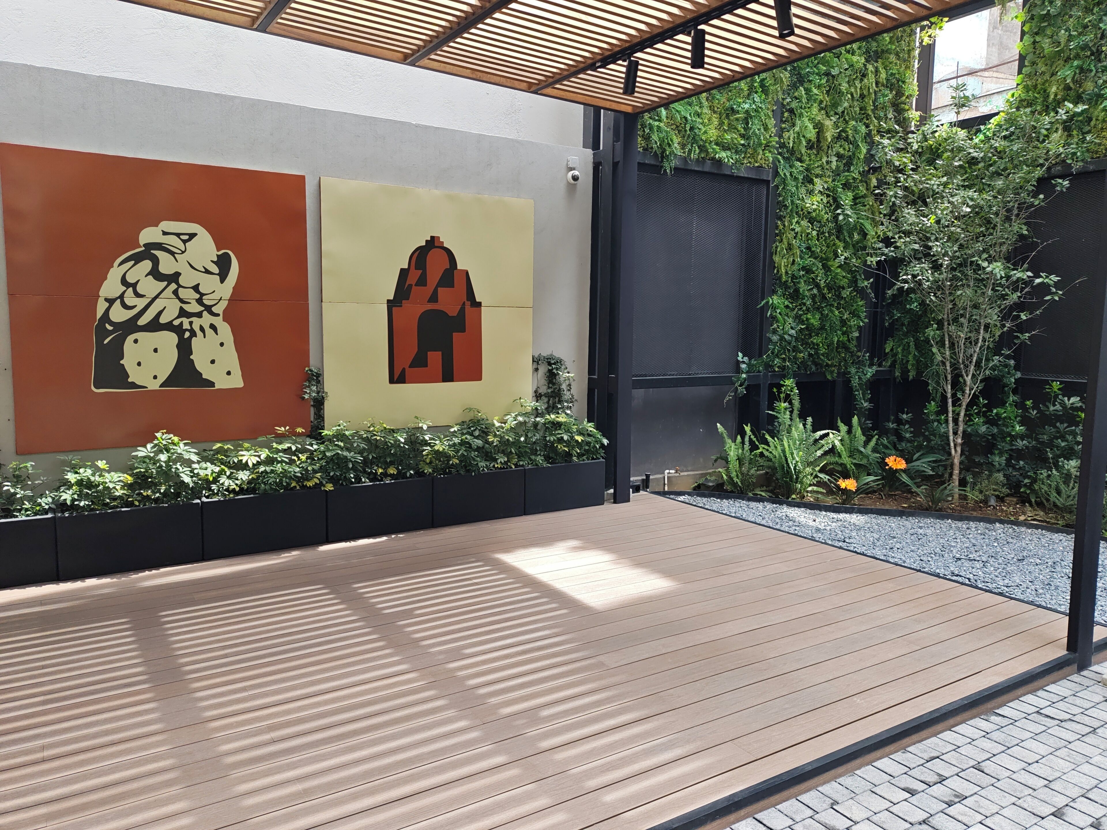 Una terrazza esterna in legno con una pergola, immersa nel verde e decorata con elementi murali.