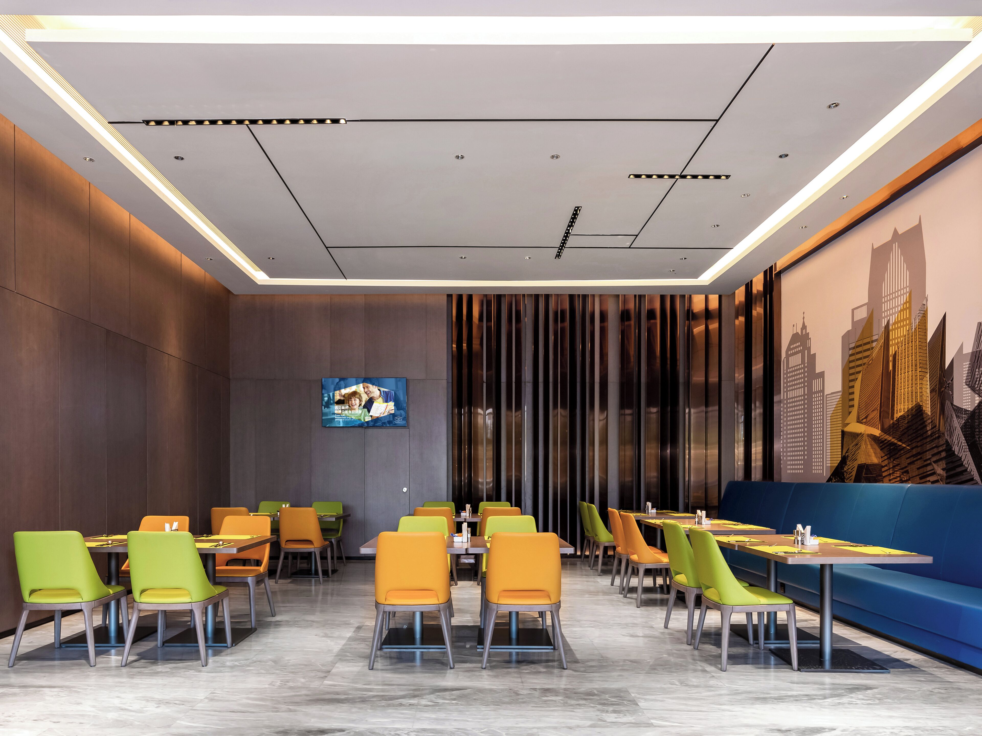 A modern restaurant with a high ceiling, recessed lighting, and a cityscape mural on the wall.