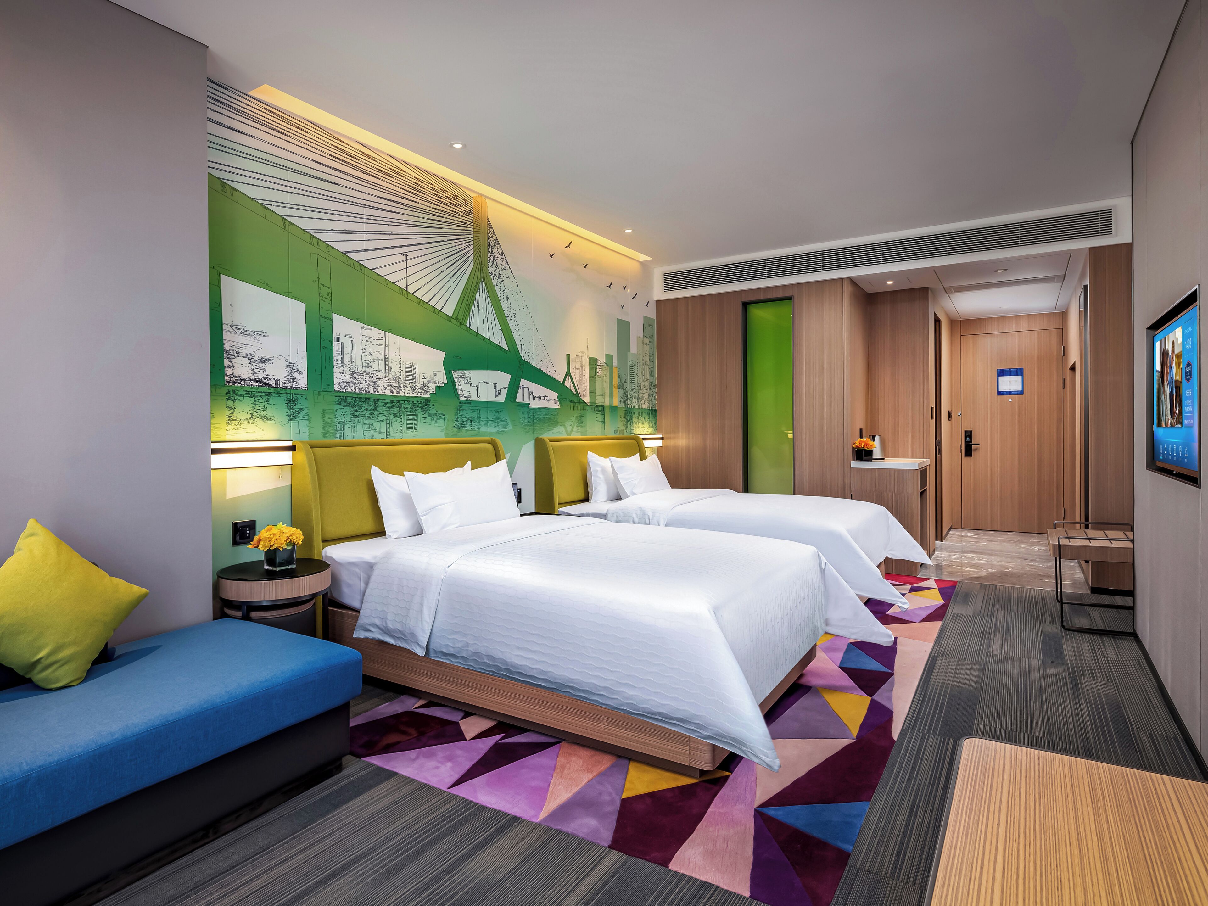 A hotel room with two beds, a sofa, a colorful rug, and a mural of a bridge.