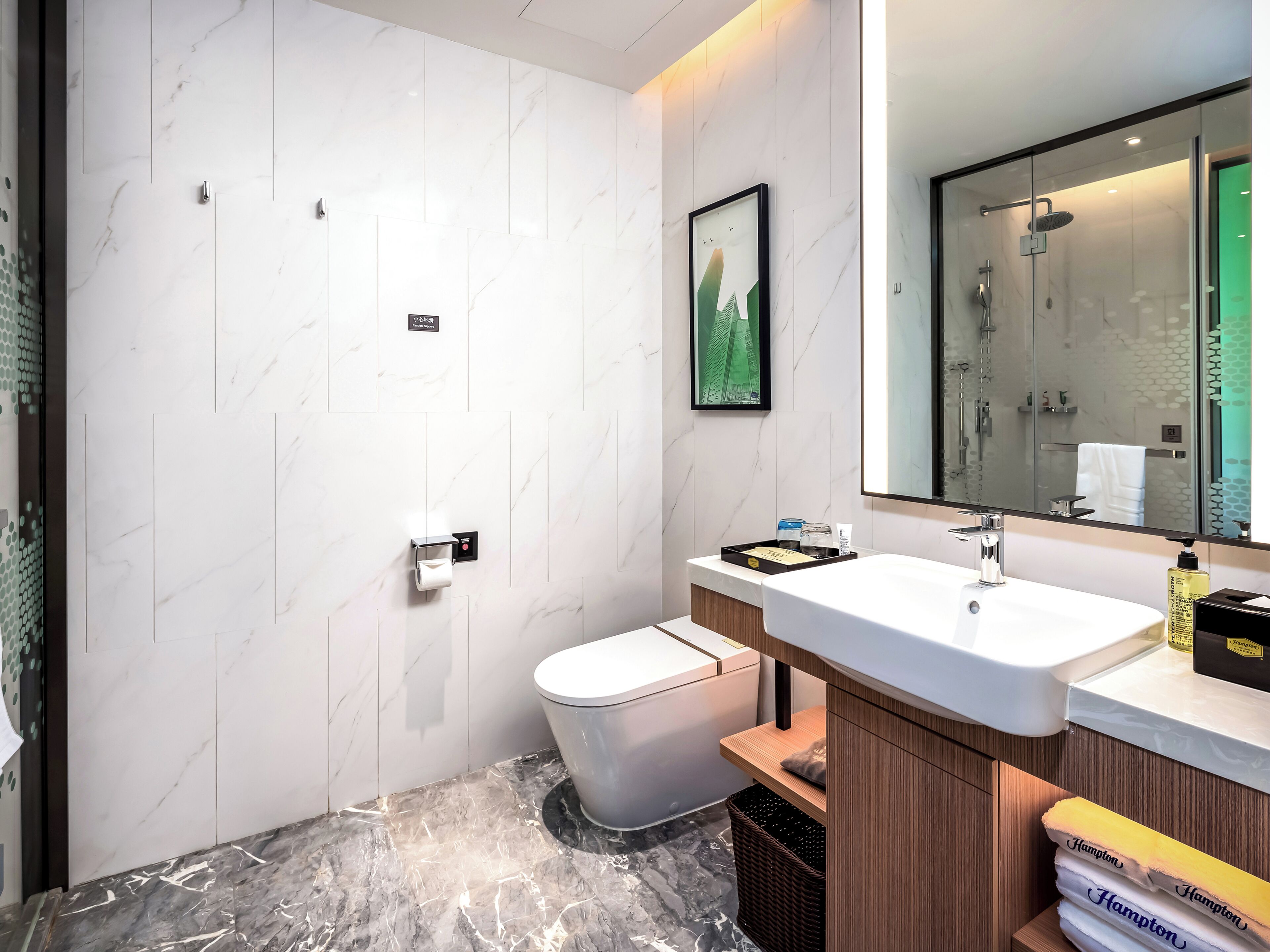 Et moderne badeværelse med en marmorvæg, toilet, vask med spejl og en bruseniche.