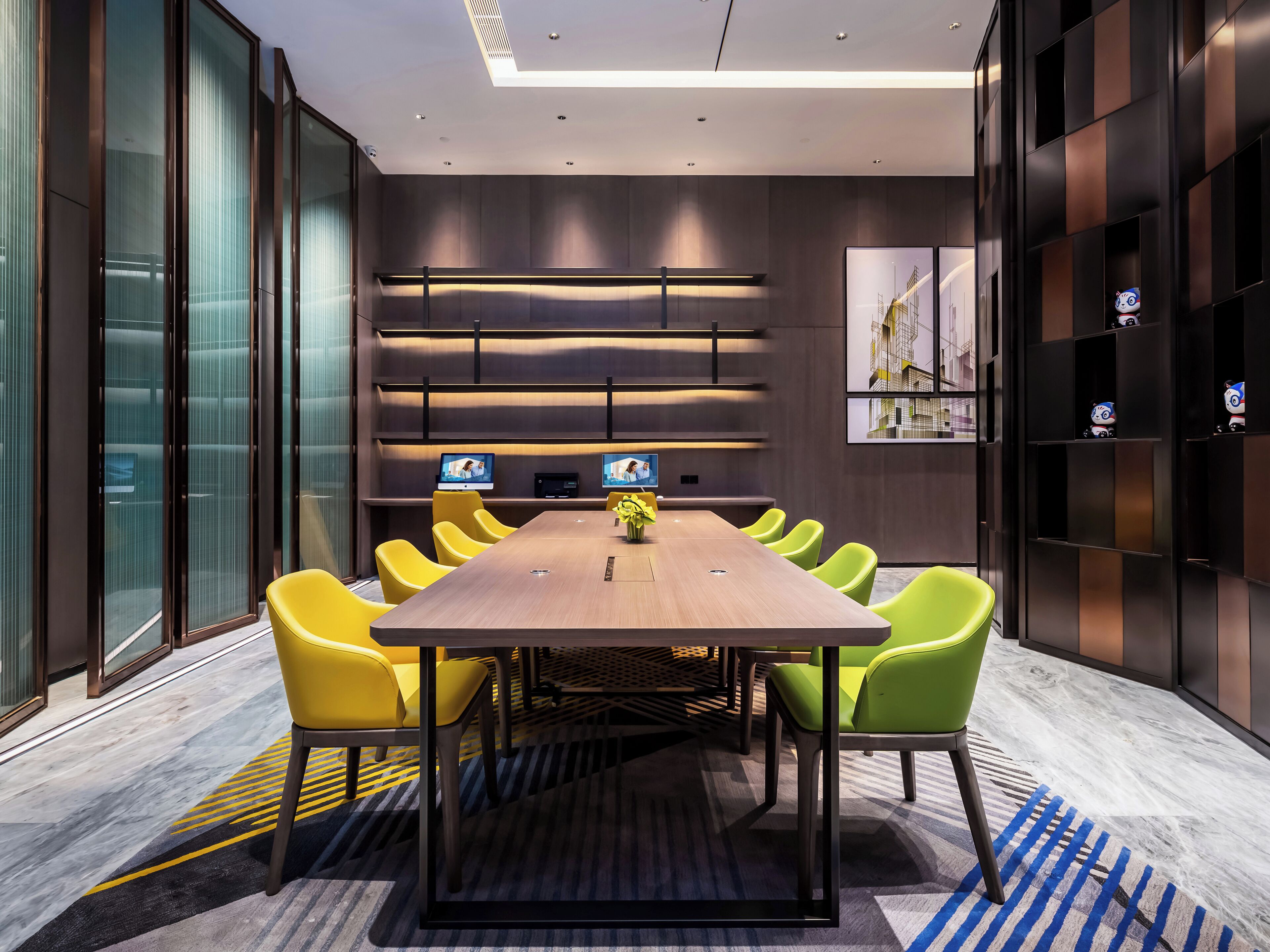 A modern meeting room with a long table, yellow chairs, and a patterned carpet.