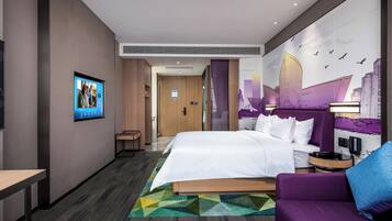 A modern hotel room with a bed, a seating area, a television, and a cityscape mural.