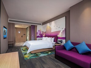 Habitación de hotel con una cama, un sofá, un televisor montado en la pared y un mural con vistas a la ciudad.