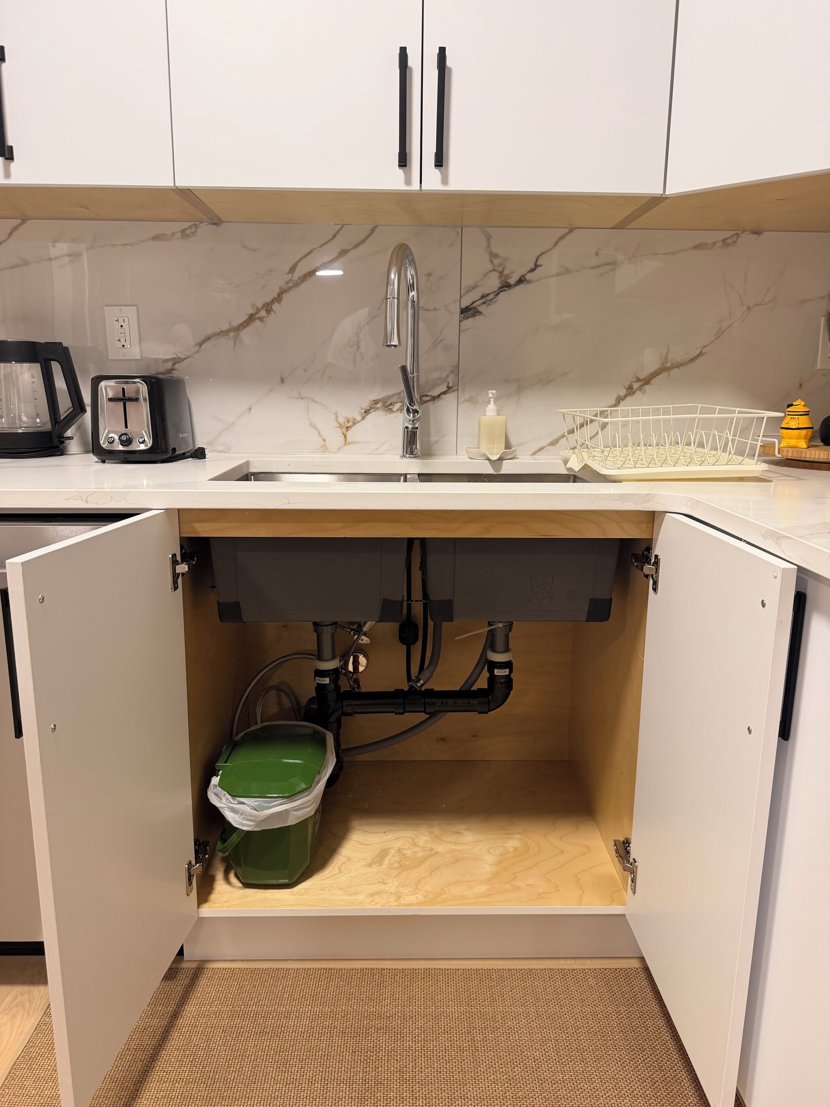 A kitchen with a built-in sink, a green trash bin, and a dish rack.