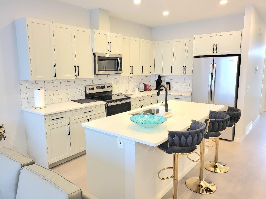 A modern kitchen with white cabinetry, a central island, and bar stools.