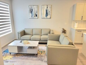 A living room with a sofa, a coffee table, and abstract art on the wall. - New 4-Bedroom Home | Modern Comfort in NE Calgary—Beautiful and Affordable (Calgary)