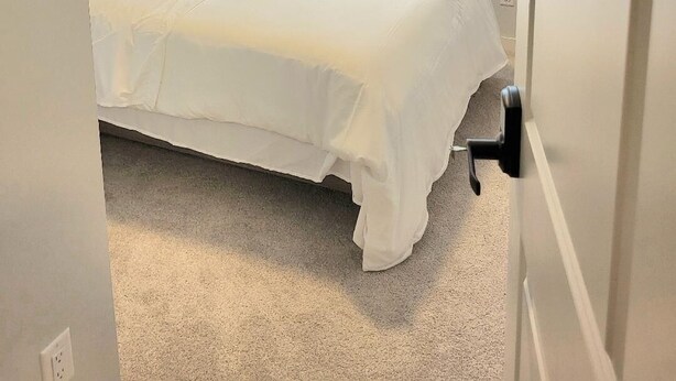 A bedroom with a bed, a window with blinds, and a door with a number. - New 4-Bedroom Home | Modern Comfort in NE Calgary—Beautiful and Affordable (Calgary)