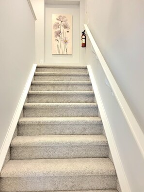 A carpeted staircase with white walls and a fire extinguisher mounted on the wall. - New 4-Bedroom Home | Modern Comfort in NE Calgary—Beautiful and Affordable (Calgary)