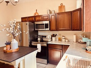 A kitchen with dark wooden cabinets, stainless steel appliances, a marble countertop, and a vase with white flowers. - Historical 1940s Bungalow Near NMSU & Mesilla (Las Cruces)