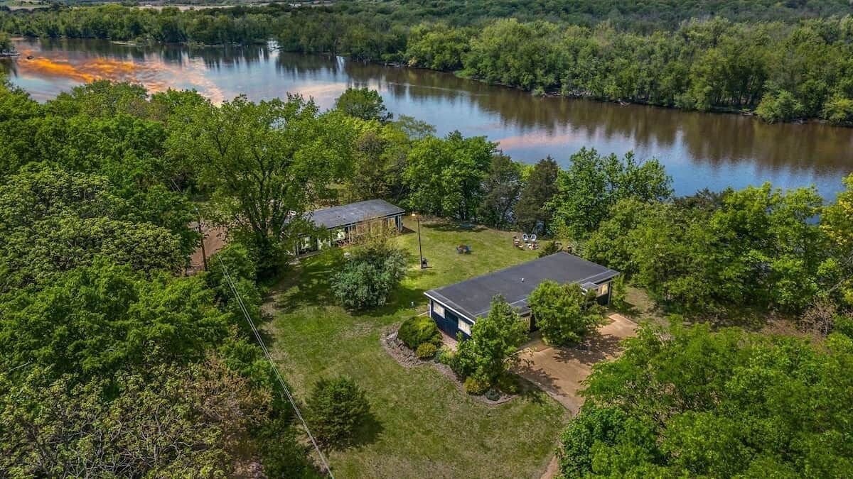 A residential property with a house and a separate building, surrounded by dense greenery and a lake.