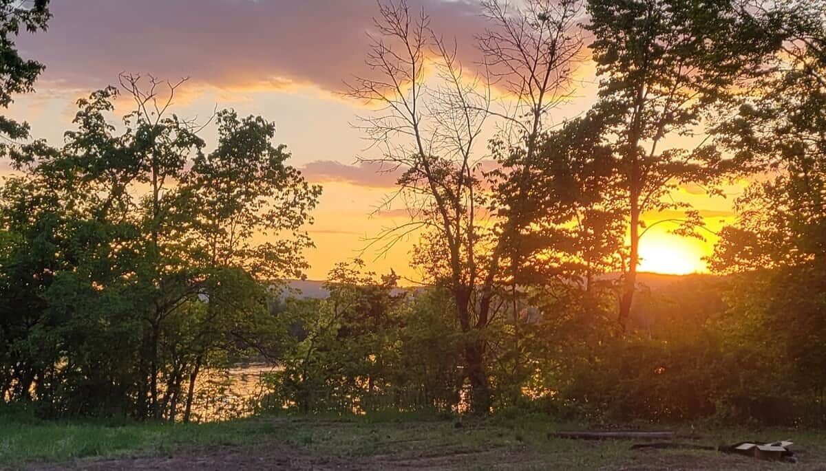 A sunset over a body of water with trees in the foreground.