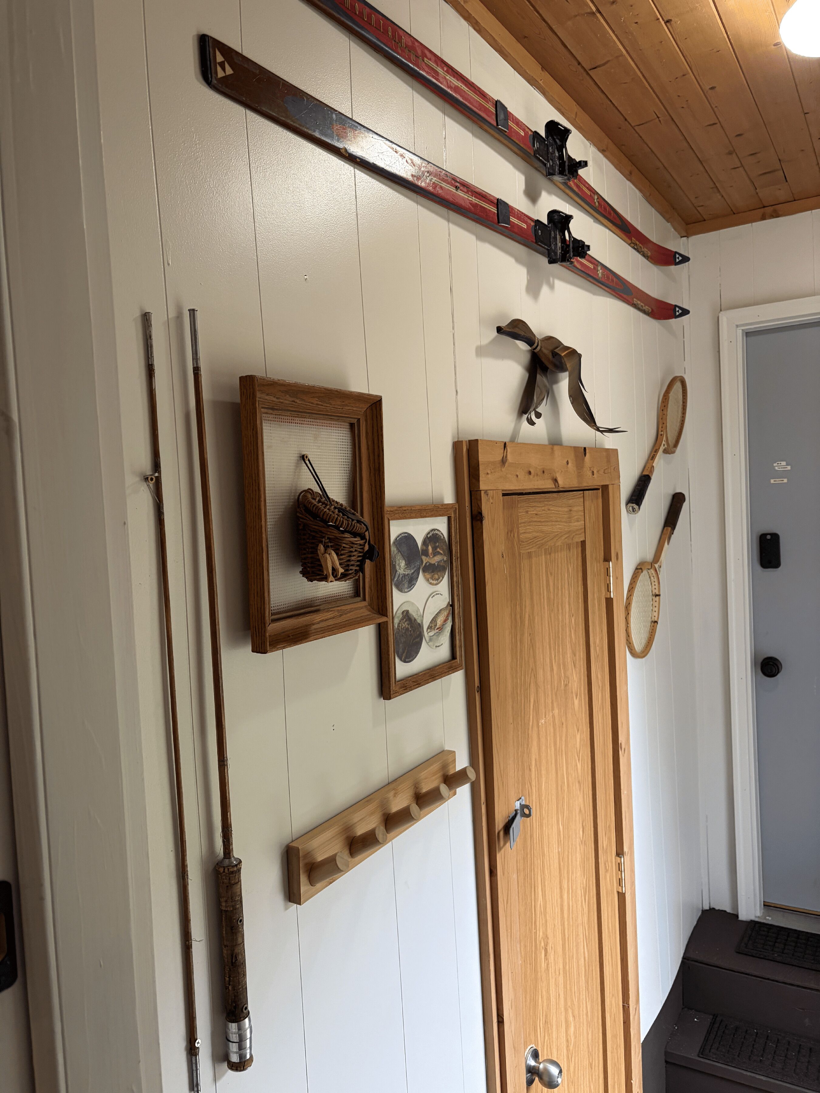 A room with a wooden door, skis, a framed picture, a rack, and a tennis racket.