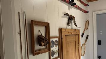 A room with a wooden door, skis, a framed picture, a rack, and a tennis racket.