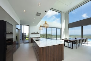 A modern kitchen with a large island, a dining area with a view, and a large window. - Starlit A Luxury Hilltop Villa with Infinity Pool (Weligama)