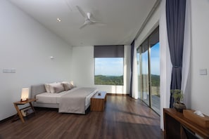 A modern bedroom with a large bed, a bedside table with a lamp, a wooden nightstand, and a view of the outdoors through a large window. - Starlit A Luxury Hilltop Villa with Infinity Pool (Weligama)