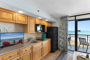 A kitchen with wooden cabinets, a black refrigerator, a microwave, and a sink. - Beachfront Condo|Private Pool, Oceanfront Balcony (North Myrtle Beach)