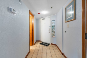 A hallway with a tiled floor, a door with a window, and a wall-mounted thermostat. - Beachfront Condo|Private Pool, Oceanfront Balcony (North Myrtle Beach)