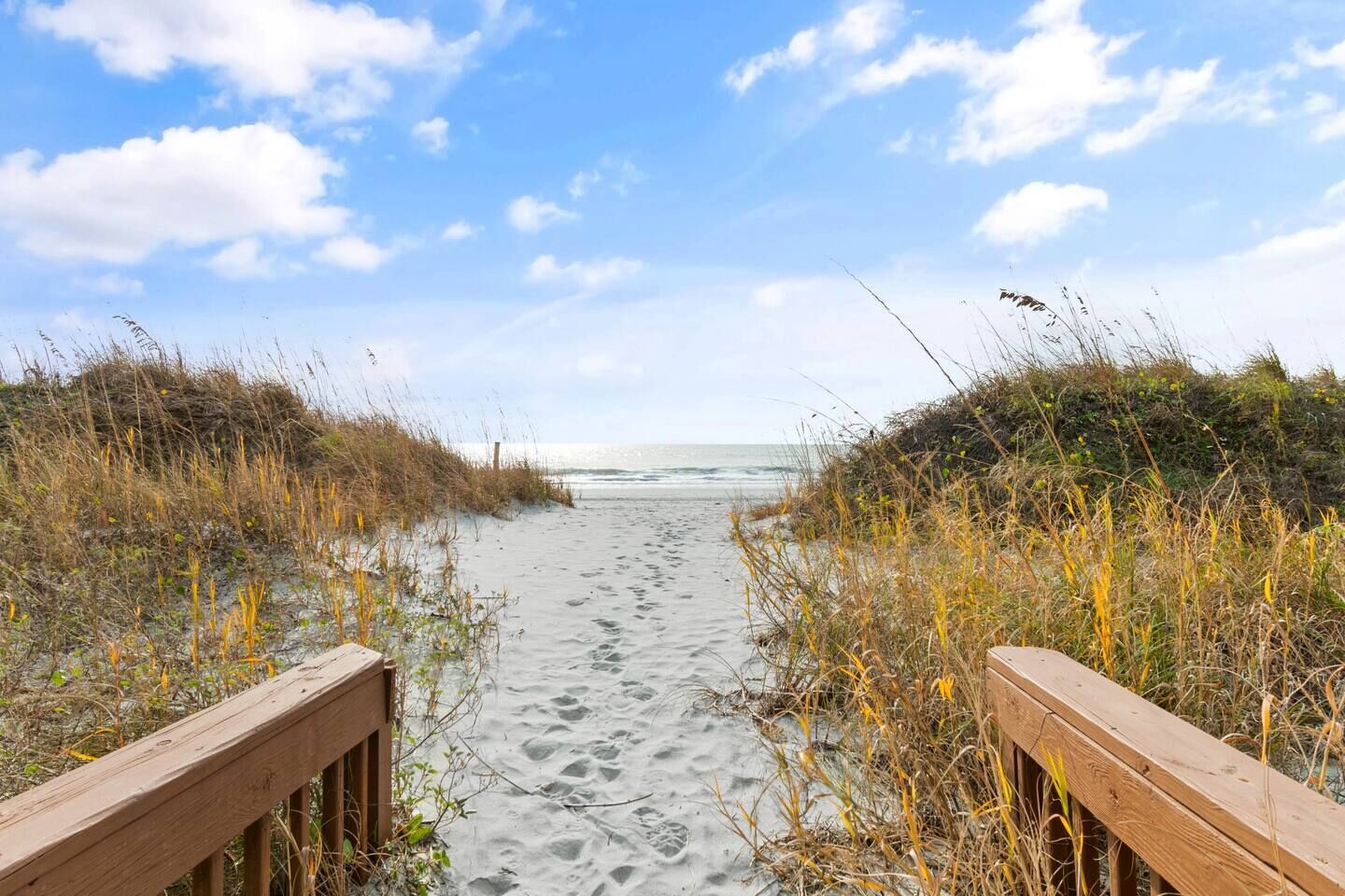 Ein Sandweg am Strand mit hölzernen Geländern, der zum Meer führt.