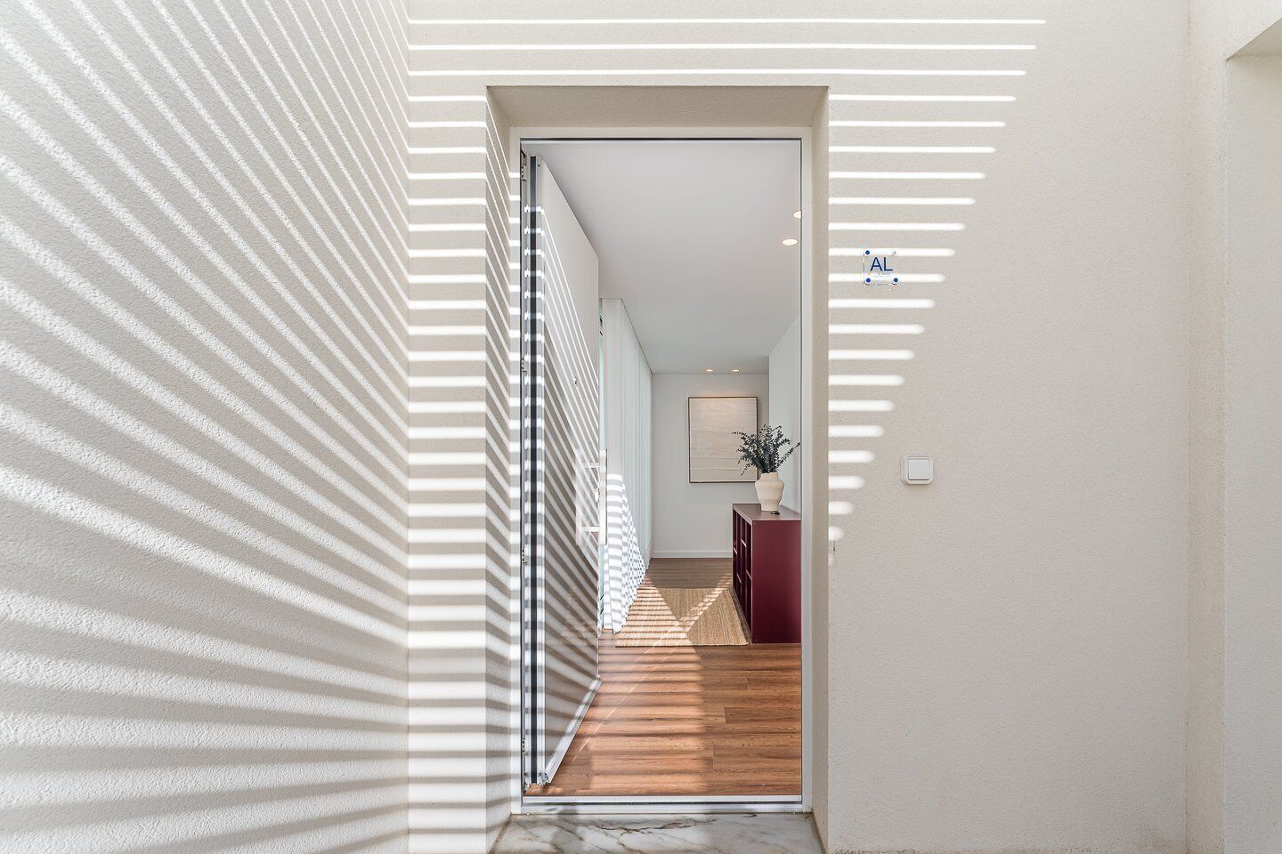 A hallway with a striped wall, a wooden floor, a red cabinet, and a plant.