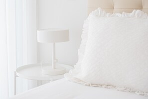 A white bed with a fluffy white blanket and a white bedside table with a lamp. - GuestReady-Modern Retreat with Private Balcony (Guimarães)