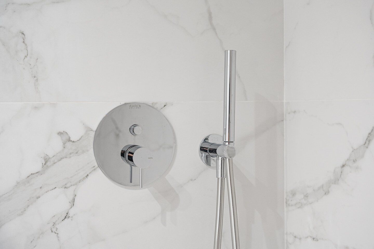 Une douche moderne dotée d’un panneau de commande mural et d’une poignée verticale.