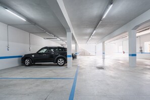 A multi-level parking garage with concrete pillars, fluorescent lighting, and blue painted lines on the floor. - GuestReady-Modern Retreat with Private Balcony (Guimarães)