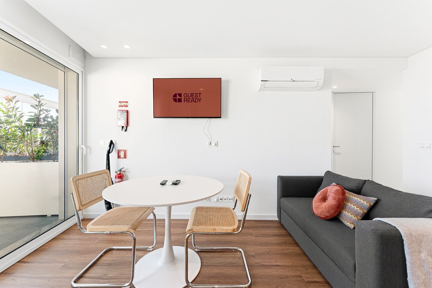 Een moderne kamer met een ronde tafel, vier stoelen, een grijze bank en een wandgemonteerde televisie.