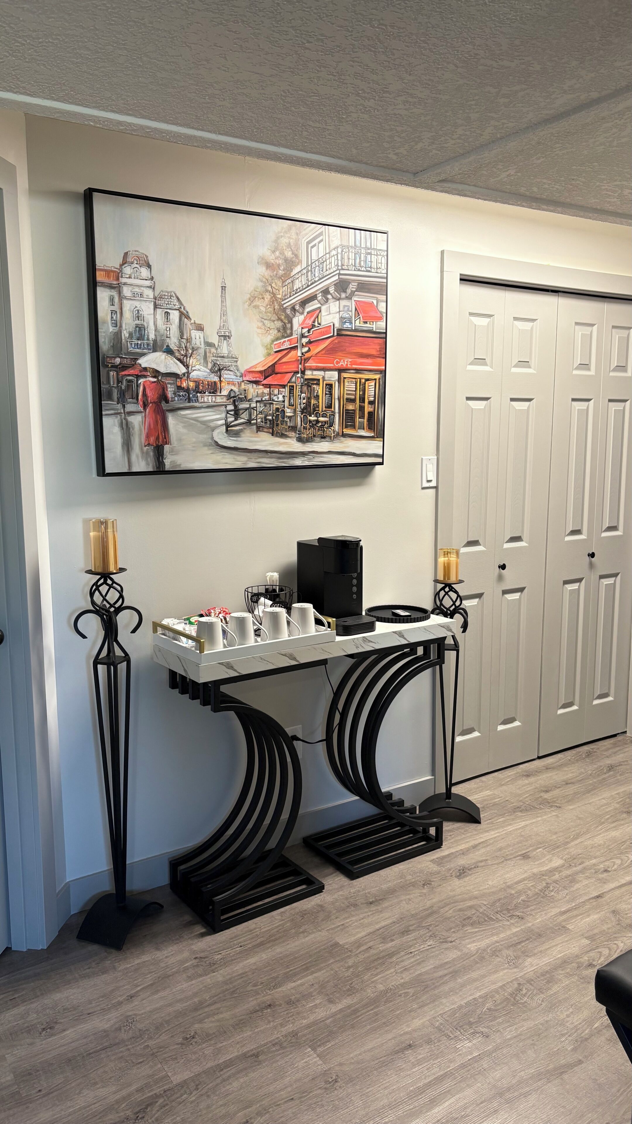 A room with a coffee station, a painting of a café scene, and a closed door.