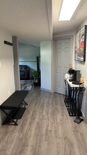 A modern living space with a bench, a coffee station, and a door leading to another room.