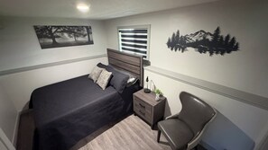 A bedroom with a bed, a nightstand, a chair, a window with blinds, and wall art. - Stylish 2 bed 1 bath basement suite (Grande Prairie)