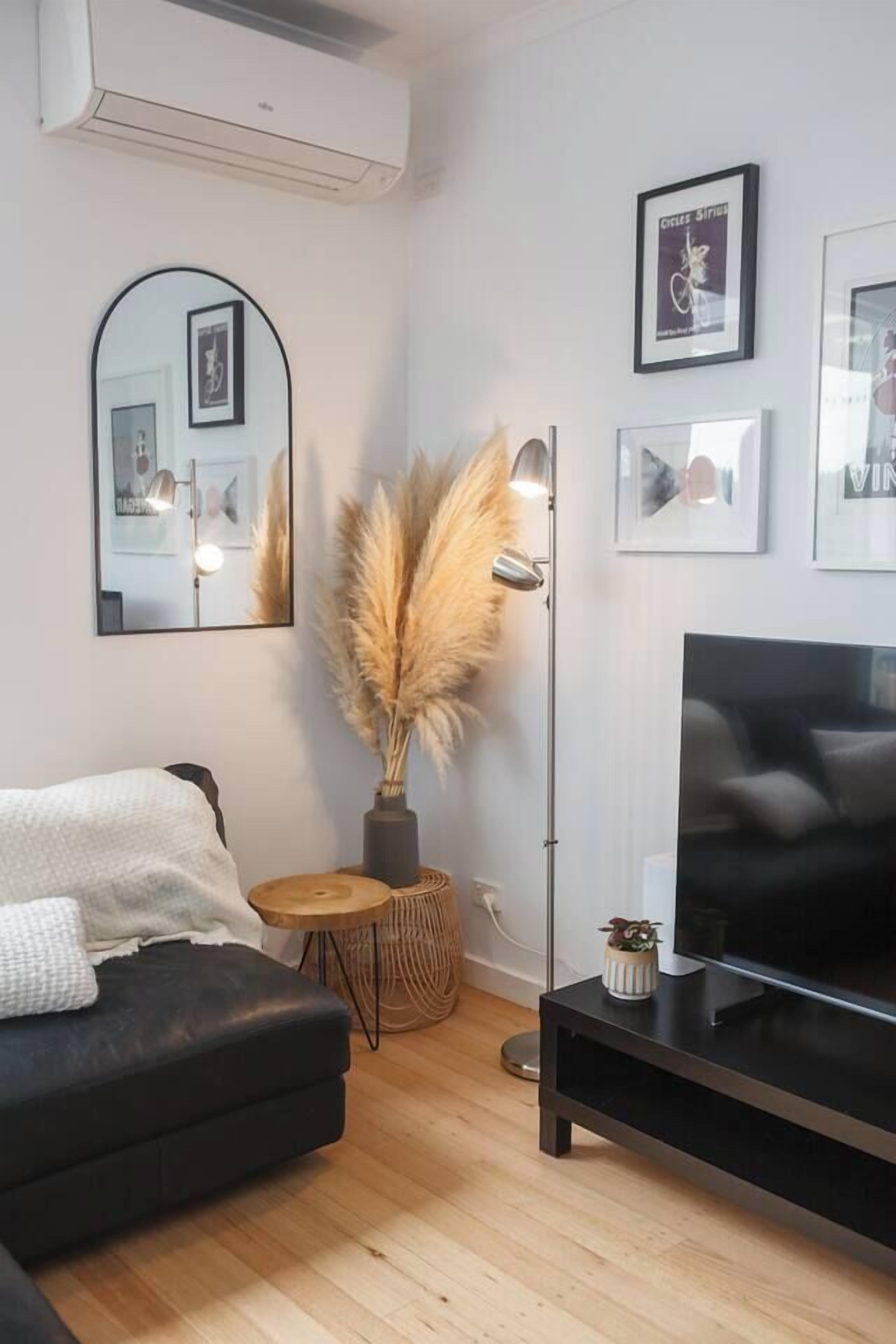 A modern living room with a black sofa, a flat-screen TV, a floor lamp, and a mirror on the wall.