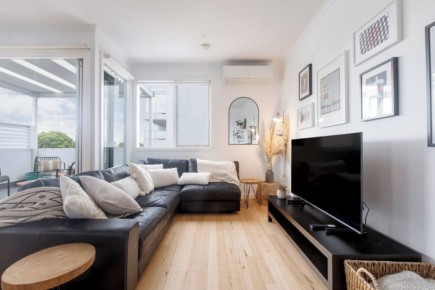 A modern living room with a sectional sofa, a flat-screen TV, and a large window offering a view of the outdoors.