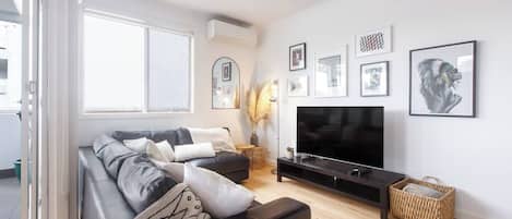 Un soggiorno moderno con un divano, una TV a schermo piatto e un'ampia finestra.