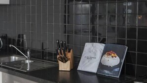 A kitchen with a black tiled backsplash, a stainless steel dishwasher, a gas stove, and a red shelf with books and a vase. - Laidback Lygon A Two Storey Inner City Oasis (Brunswick East)