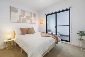 A bedroom with a bed, a nightstand, a wall-mounted lamp, and a sliding glass door leading to an outdoor area. - Laidback Lygon A Two Storey Inner City Oasis (Brunswick East)