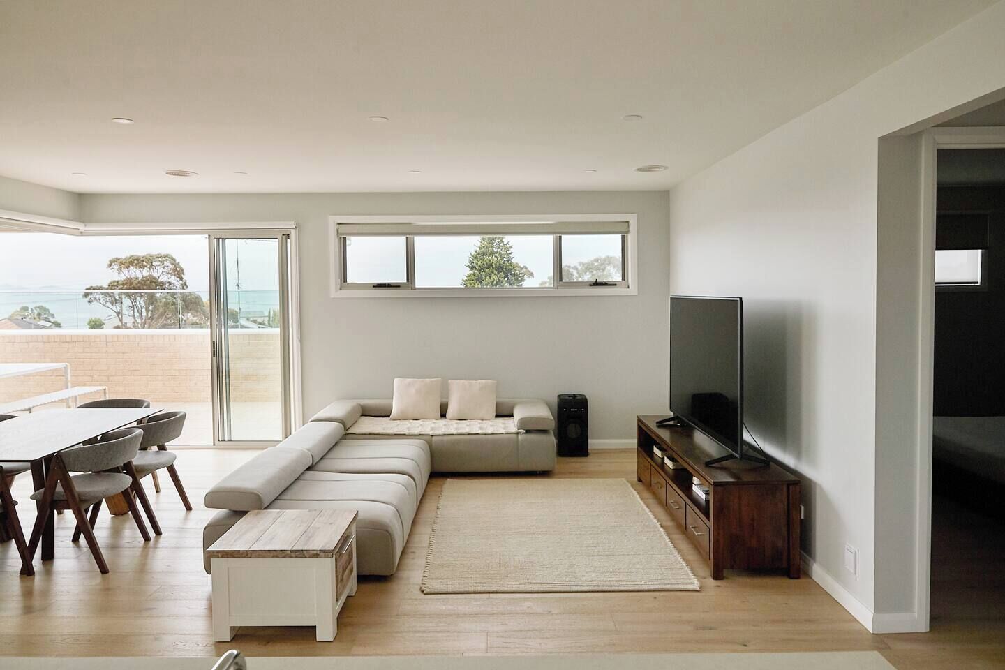 Una sala de estar moderna con un amplio sofá modular, un televisor y un comedor con una mesa y sillas.