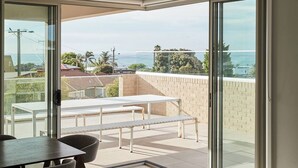 Ein moderner Balkon mit Tisch, Stühlen und einer Bank, mit Blick auf das Meer und die umliegende Landschaft.