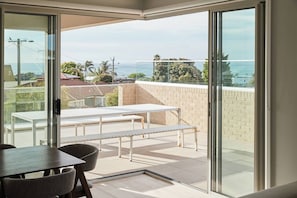 Ein moderner Balkon mit Tisch, Stühlen und einer Bank, mit Blick auf das Meer und die umliegende Landschaft.