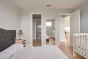 A bedroom with a large bed, a bedside table with a lamp, and a crib. There are open doors leading to other rooms. - Harbour Horizons Balcony BBQs and Calm Water Views (Clifton Springs)