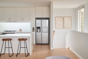 Eine moderne Küche mit weißen Schränken, einem Edelstahl-Kühlschrank und einer Bar mit Hockern.