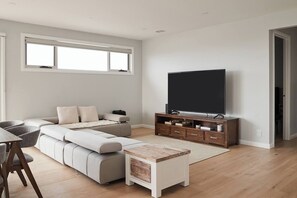 Een moderne woonkamer met een hoekbank, een flatscreen televisie op een houten standaard, en een kleine salontafel.